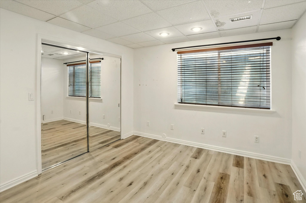 Unfurnished bedroom featuring a drop ceiling, wood finished floors, baseboards, and a closet