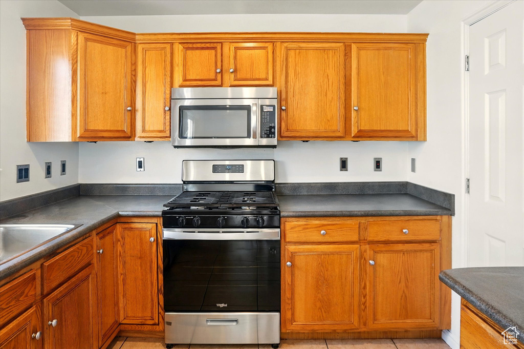 Kitchen featuring appliances with stainless steel finishes, dark countertops, brown cabinetry, and a sink