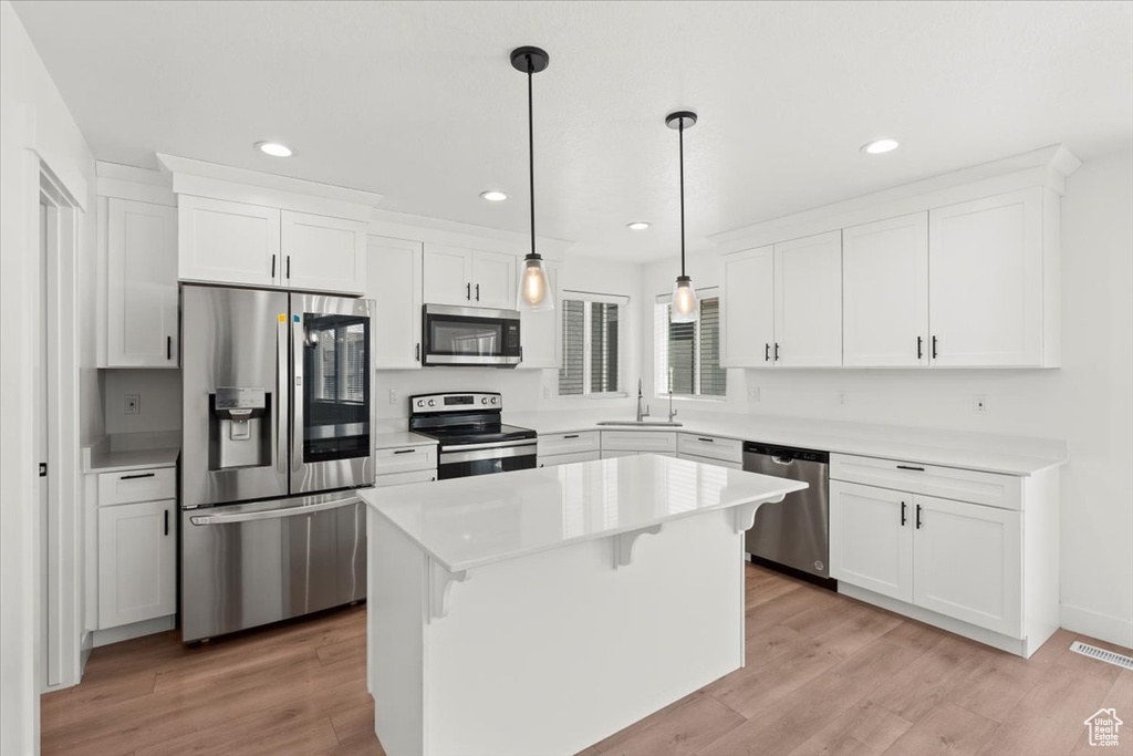 Kitchen with stainless steel appliances, a sink, recessed lighting, white cabinets, and light wood-type flooring