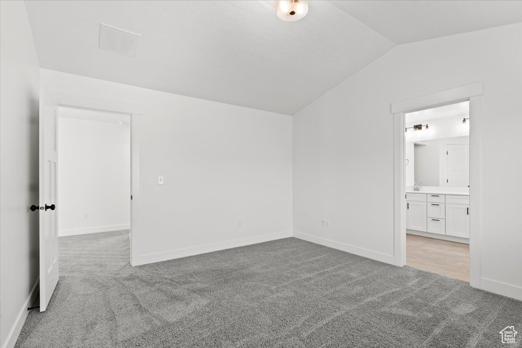 Unfurnished bedroom with light carpet, vaulted ceiling, baseboards, and connected bathroom