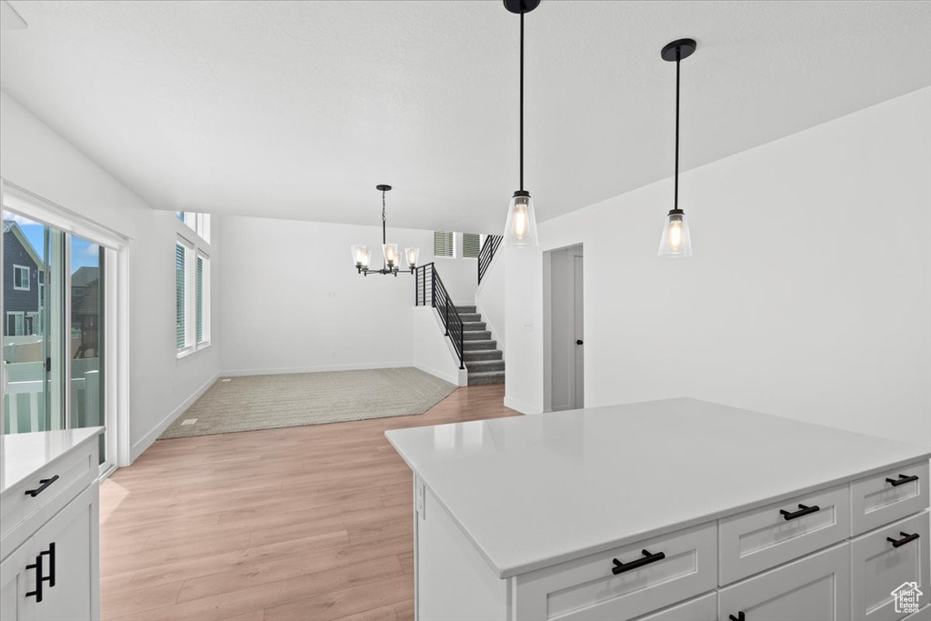 Kitchen with light wood-type flooring, light countertops, a chandelier, hanging light fixtures, and white cabinets