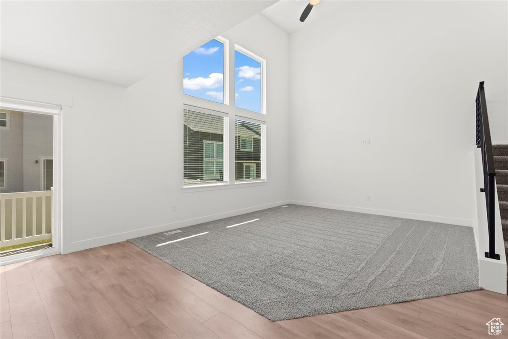 Unfurnished room featuring a ceiling fan, wood finished floors, vaulted ceiling, baseboards, and stairs