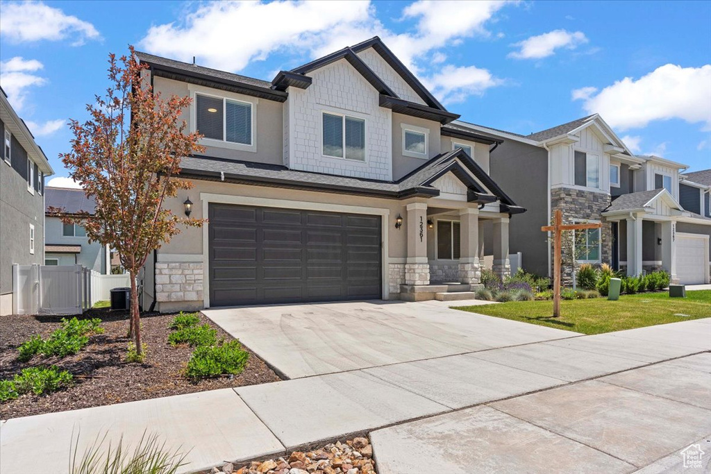 View of front facade featuring stone siding, driveway, an attached garage, stucco siding, and central air condition unit