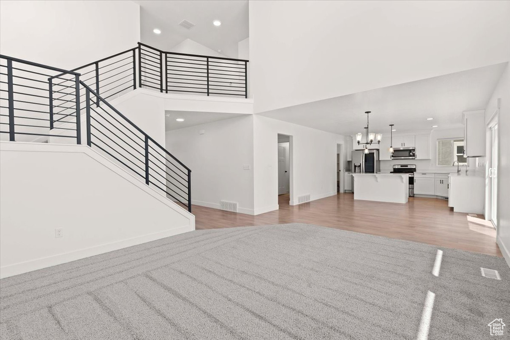 Unfurnished living room featuring a chandelier, a high ceiling, stairs, baseboards, and recessed lighting