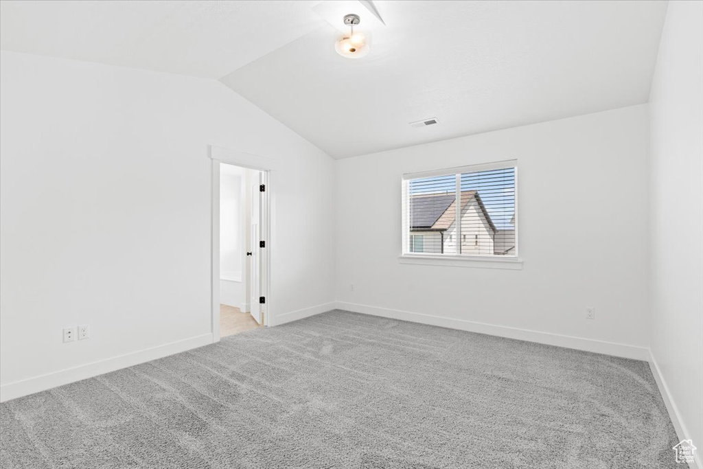 Carpeted spare room featuring lofted ceiling and baseboards
