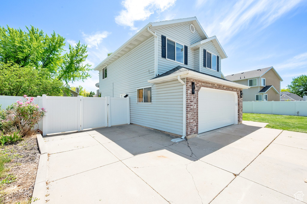 View of side of home featuring a garage, driveway, a gate, and brick siding