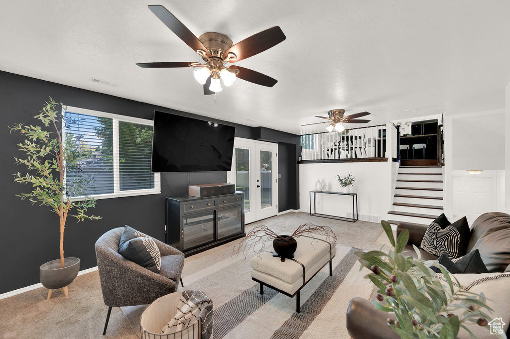 Carpeted living area featuring french doors, stairs, a ceiling fan, and baseboards
