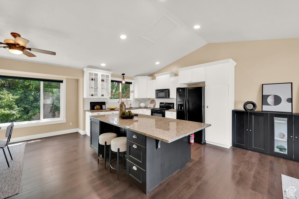Kitchen featuring black appliances, a center island, white cabinets, light stone countertops, and a kitchen bar