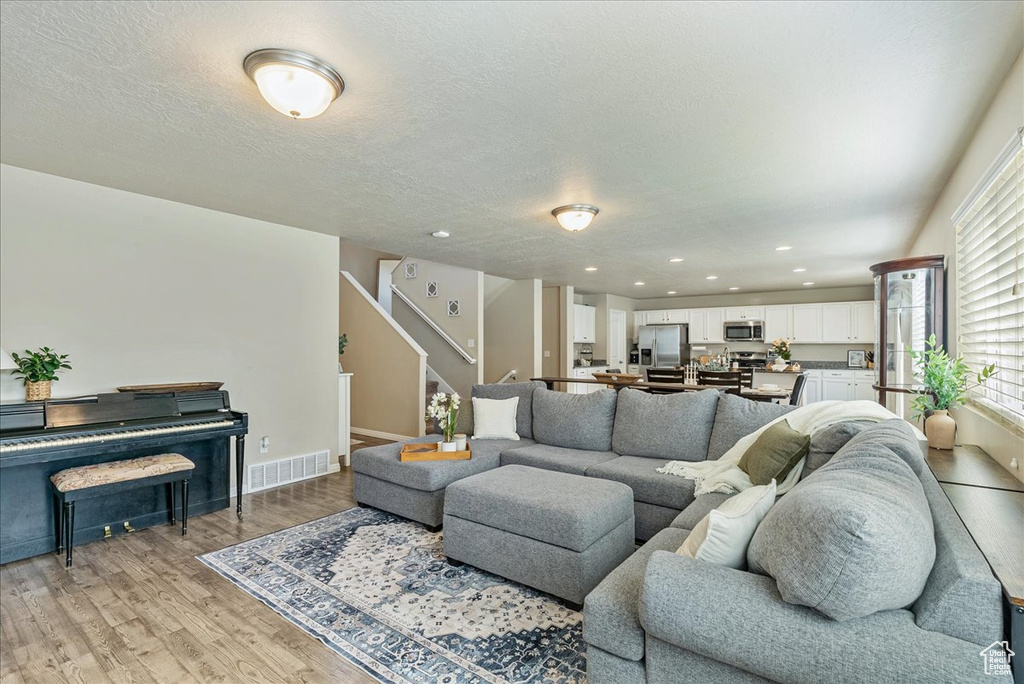 Living area with light wood-style floors, stairs, baseboards, recessed lighting, and a textured ceiling