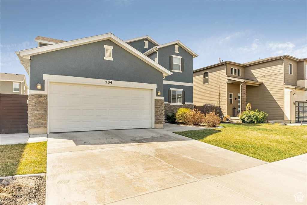 View of front facade featuring driveway, stone siding, a front lawn, and an attached garage