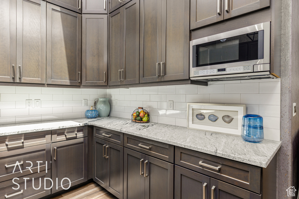 Kitchen featuring stainless steel microwave, dark brown cabinetry, decorative backsplash, and light stone countertops
