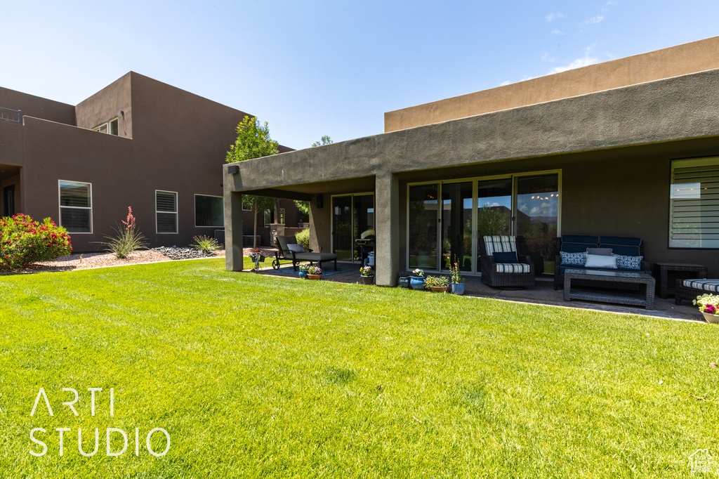 Back of house with an outdoor living space, a patio, a lawn, and stucco siding