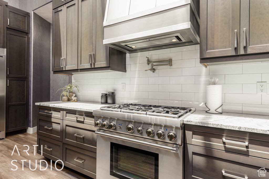 Kitchen with premium appliances, custom range hood, backsplash, and wood finished floors
