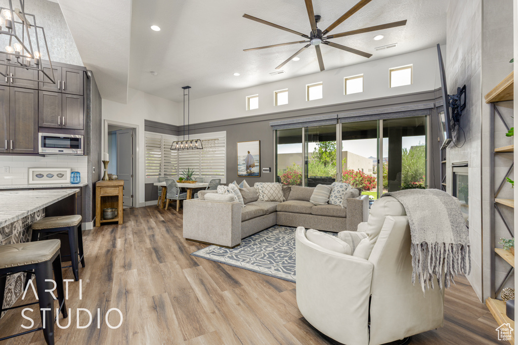 Living area featuring a chandelier, a ceiling fan, recessed lighting, a high ceiling, and light wood-style floors