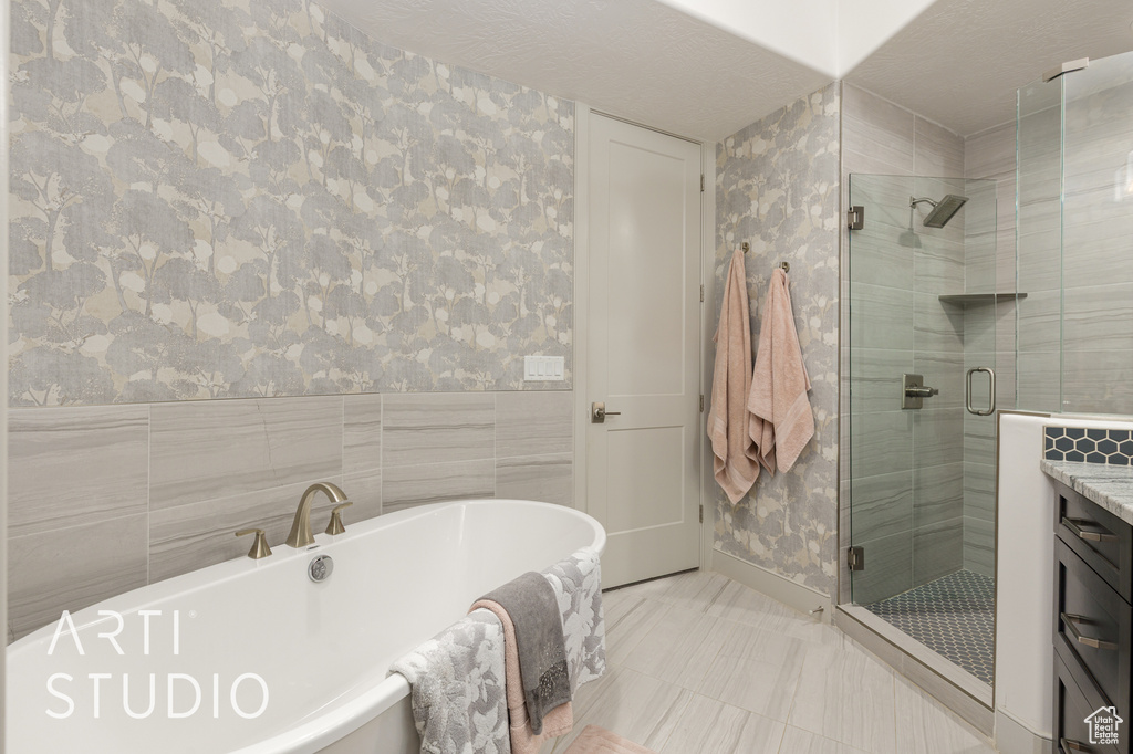 Bathroom featuring wallpapered walls, a shower stall, a freestanding tub, and vanity