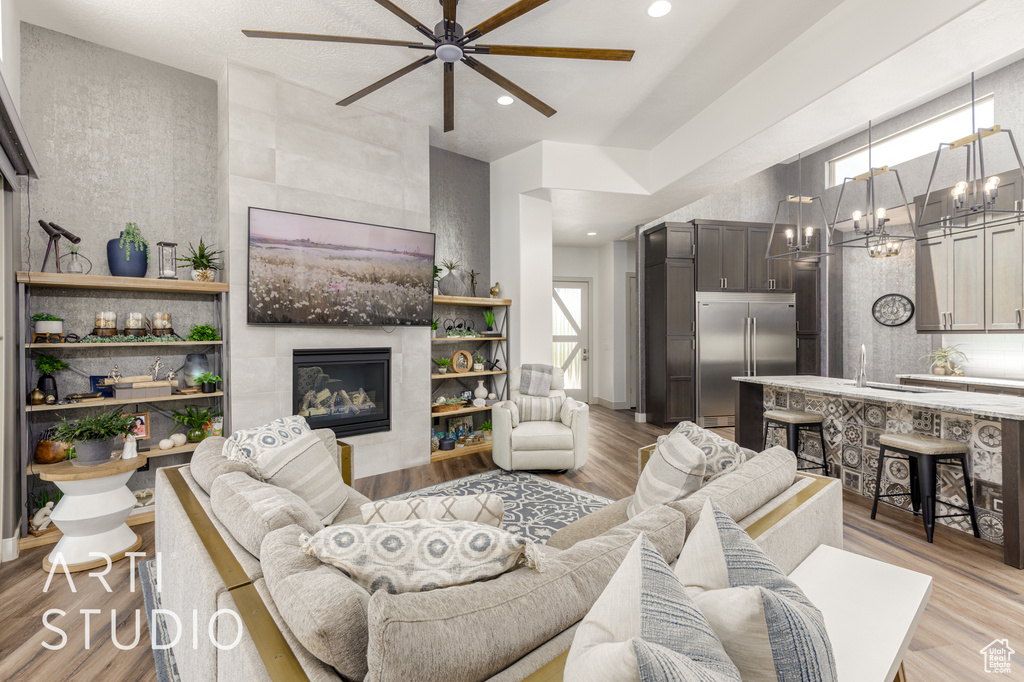 Living area with a ceiling fan, a fireplace, recessed lighting, a chandelier, and light wood-style flooring