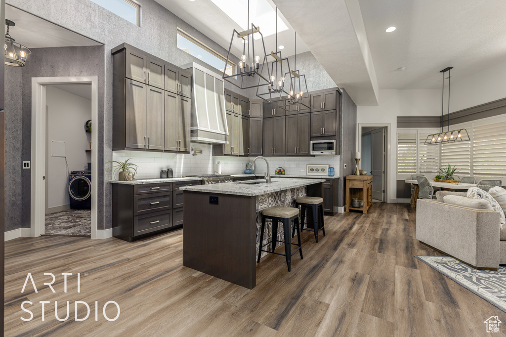 Kitchen with appliances with stainless steel finishes, a chandelier, a sink, a breakfast bar, and backsplash