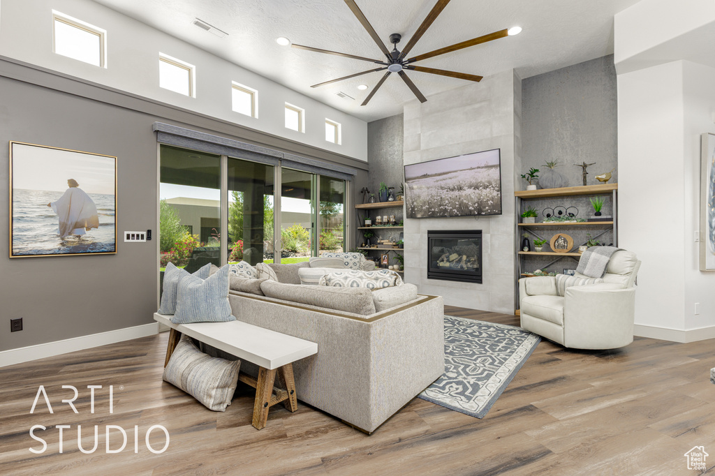 Living room featuring a tiled fireplace, recessed lighting, a high ceiling, baseboards, and wood finished floors