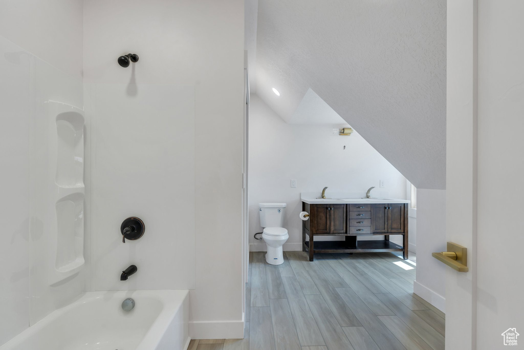 Bathroom featuring baseboards, toilet, double vanity, wood finished floors, and vaulted ceiling