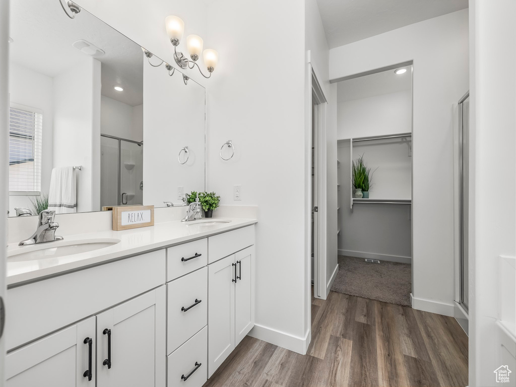 Full bathroom with a shower stall, double vanity, wood finished floors, baseboards, and a closet