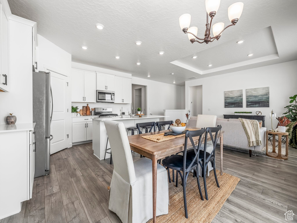 Dining area with wood finished floors, a chandelier, recessed lighting, a textured ceiling, and a raised ceiling