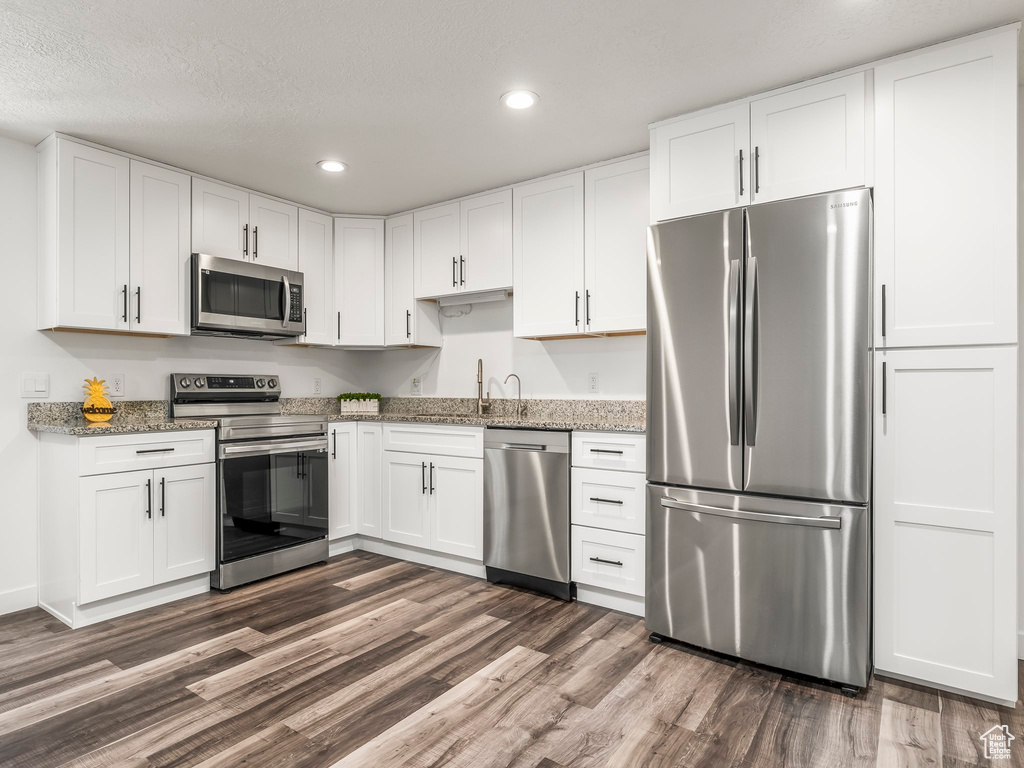 Kitchen with appliances with stainless steel finishes, recessed lighting, dark wood-style flooring, white cabinetry, and light stone countertops