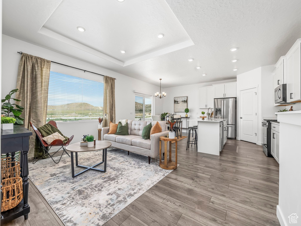 Living room with a chandelier, recessed lighting, wood finished floors, and a raised ceiling