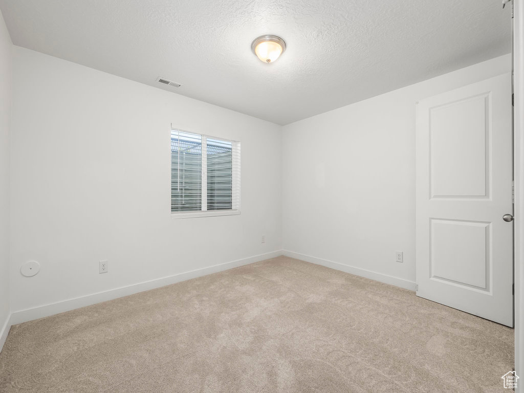 Empty room with light colored carpet, baseboards, and a textured ceiling