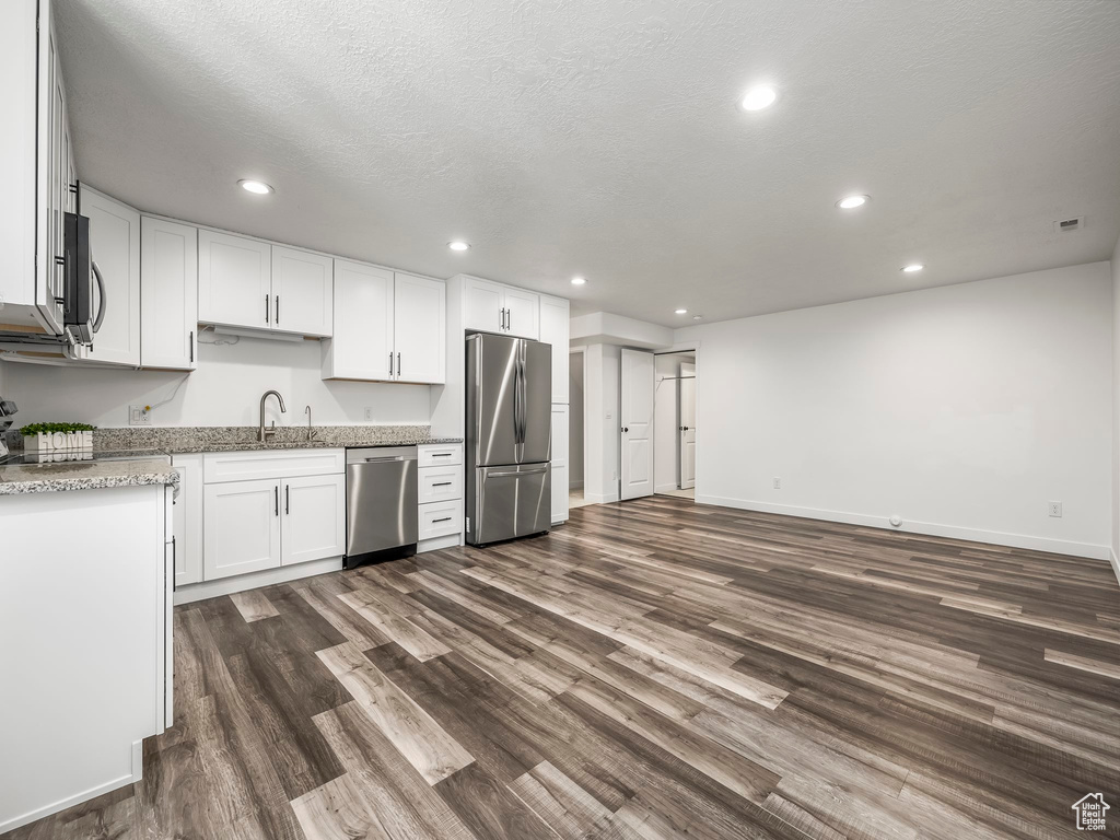 Kitchen with appliances with stainless steel finishes, dark wood finished floors, a sink, white cabinets, and recessed lighting