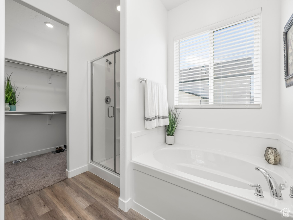 Full bath featuring a shower stall, a garden tub, a walk in closet, wood finished floors, and baseboards