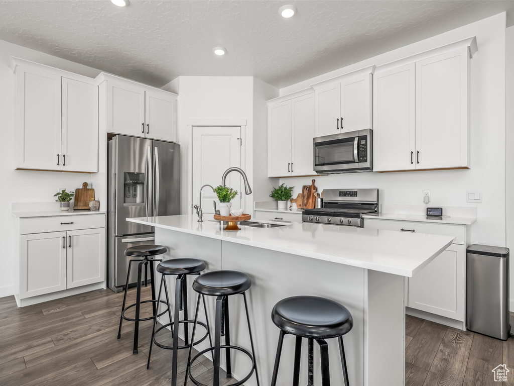 Kitchen with stainless steel appliances, dark wood-style flooring, recessed lighting, a breakfast bar area, and white cabinets