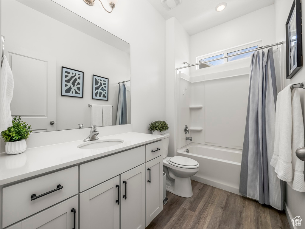 Bathroom featuring vanity, toilet, shower / tub combo, and wood finished floors