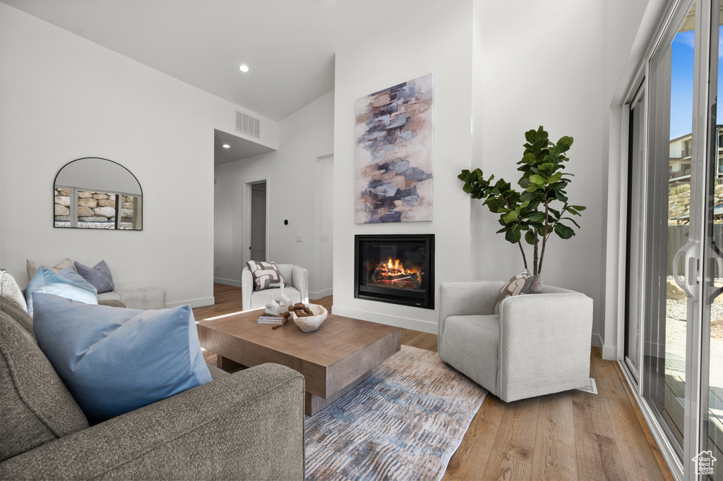 Living area with wood finished floors, a glass covered fireplace, a high ceiling, baseboards, and recessed lighting