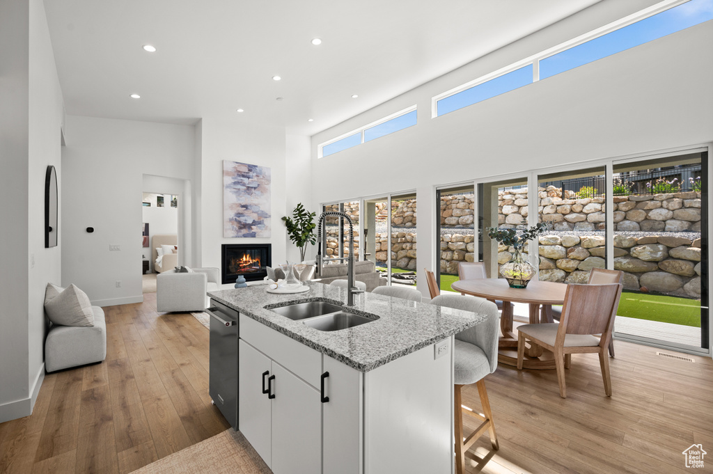 Kitchen with a sink, a warm lit fireplace, open floor plan, a center island with sink, and light wood-type flooring