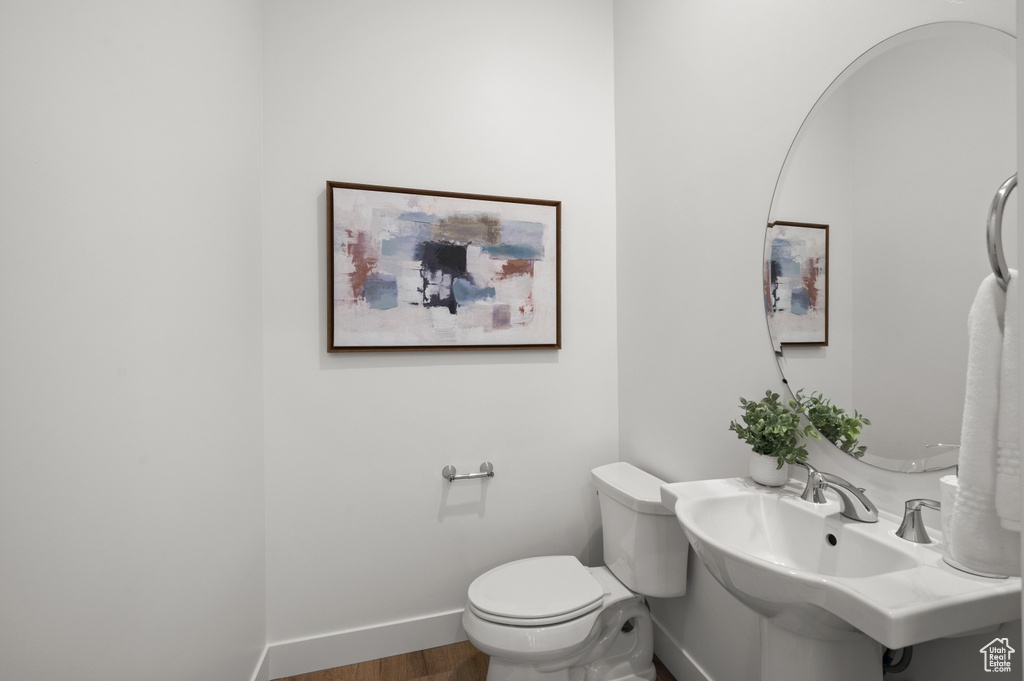 Half bathroom with baseboards, wood finished floors, toilet, and a sink
