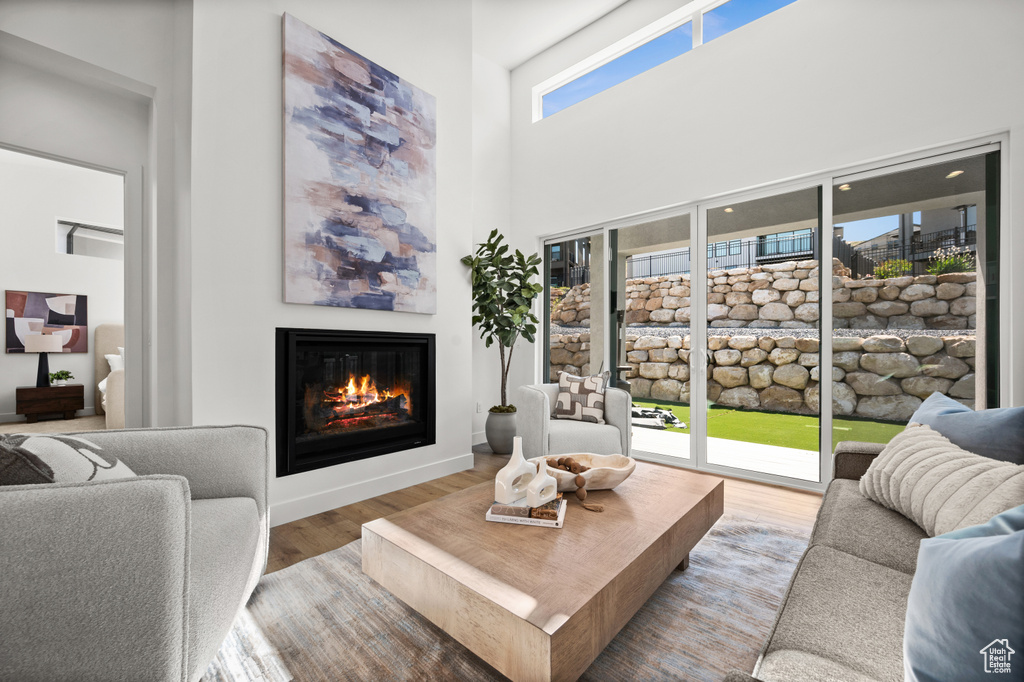 Living area with a glass covered fireplace, wood finished floors, and a high ceiling