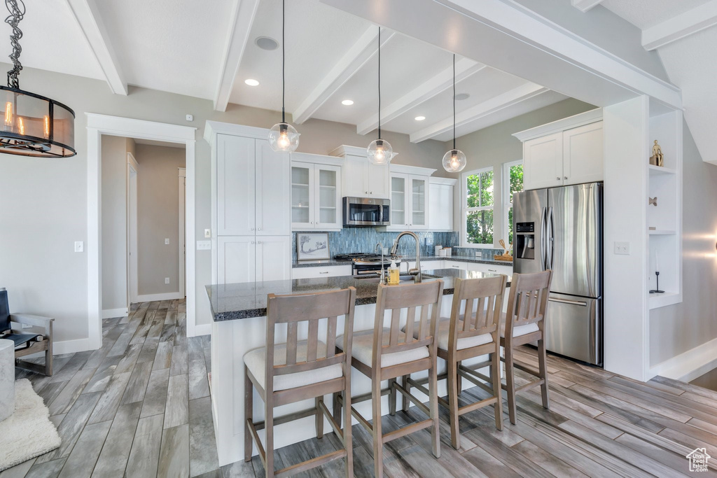 Kitchen featuring stainless steel appliances, beamed ceiling, light wood-type flooring, decorative backsplash, and white cabinets