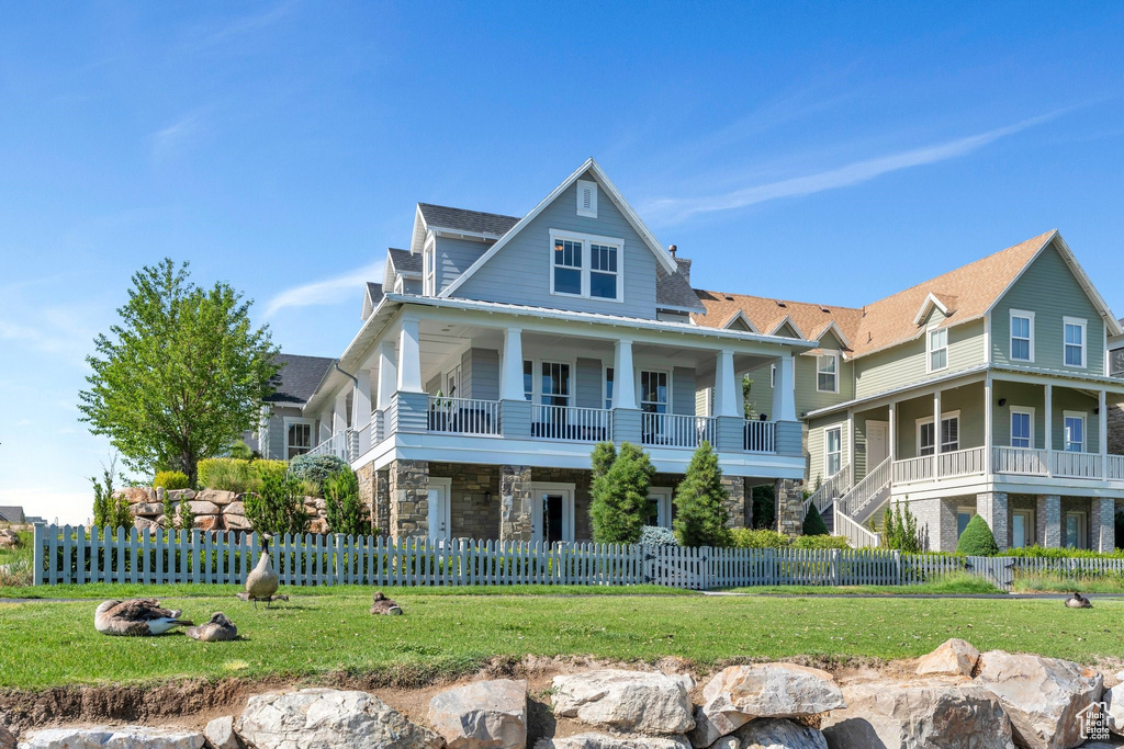 View of front of house with stone siding, a fenced front yard, and a balcony