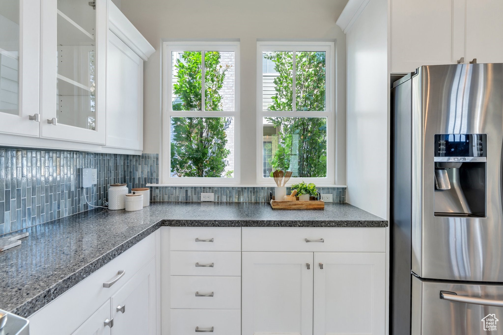 Kitchen featuring stainless steel refrigerator with ice dispenser, backsplash, glass insert cabinets, and white cabinetry