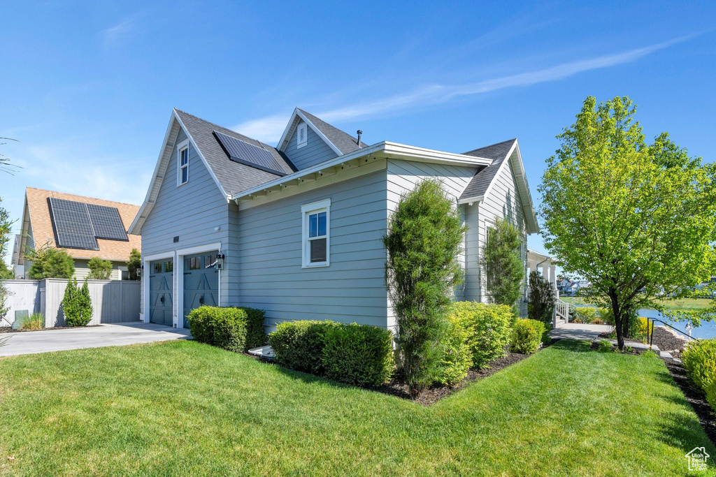 View of home's exterior with solar panels, concrete driveway, an attached garage, and a shingled roof