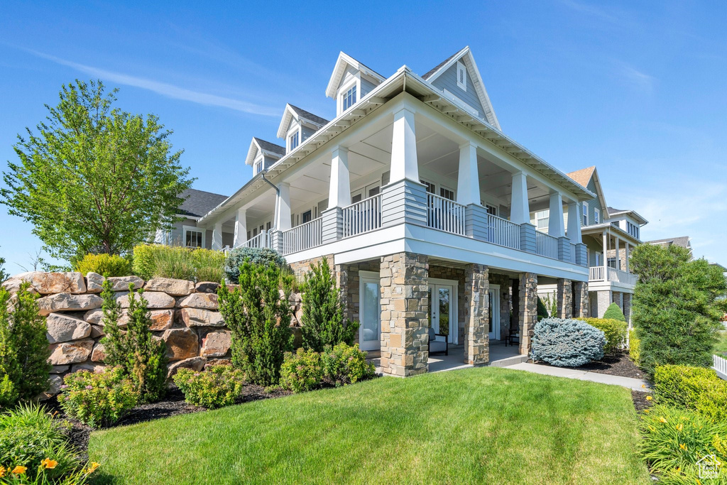 Rear view of property featuring stone siding, a lawn, and a balcony
