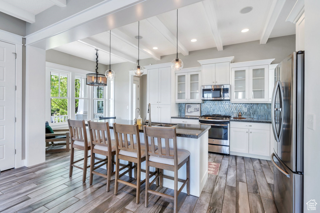 Kitchen with stainless steel appliances, beamed ceiling, wood finished floors, a sink, and white cabinets