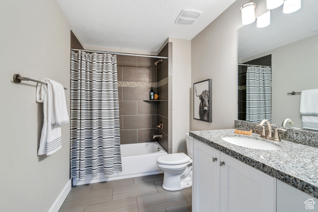 Full bathroom with vanity, toilet, shower / tub combo, a textured ceiling, and baseboards