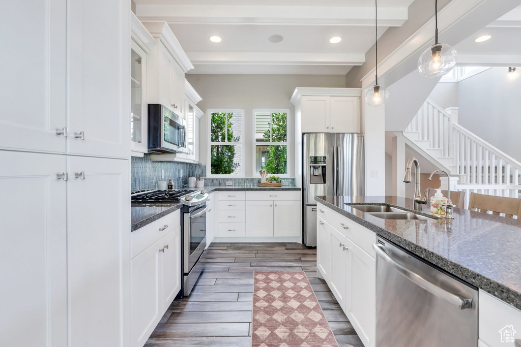 Kitchen with stainless steel appliances, a sink, wood finished floors, dark stone counters, and decorative light fixtures
