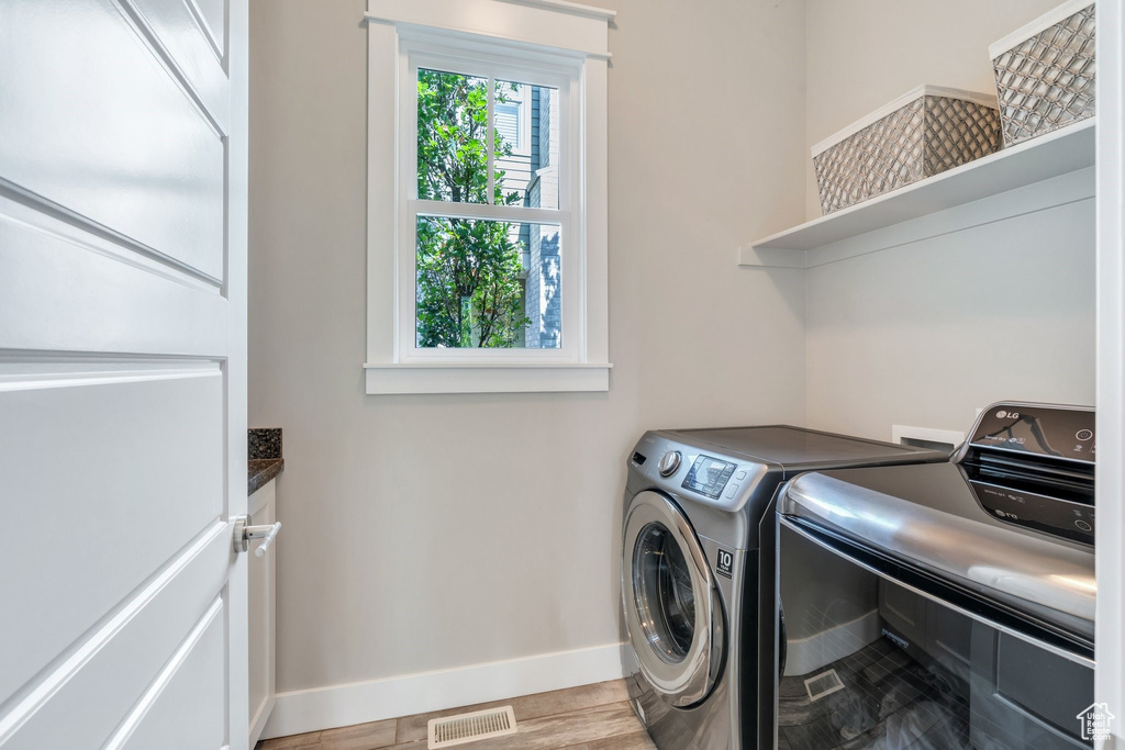 Washroom with washer and clothes dryer, baseboards, cabinet space, and light wood finished floors
