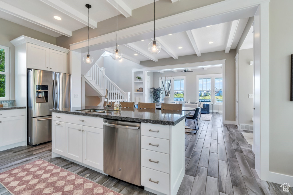 Kitchen with stainless steel appliances, a sink, open floor plan, beam ceiling, and wood finished floors