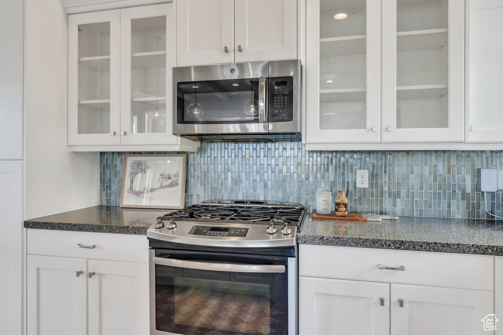 Kitchen with appliances with stainless steel finishes, white cabinets, and glass insert cabinets