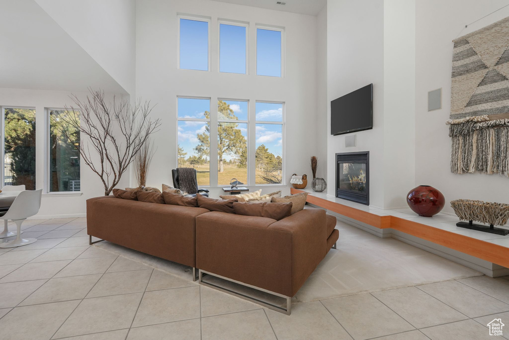 Living area with a towering ceiling, light tile patterned floors, a glass covered fireplace, and plenty of natural light