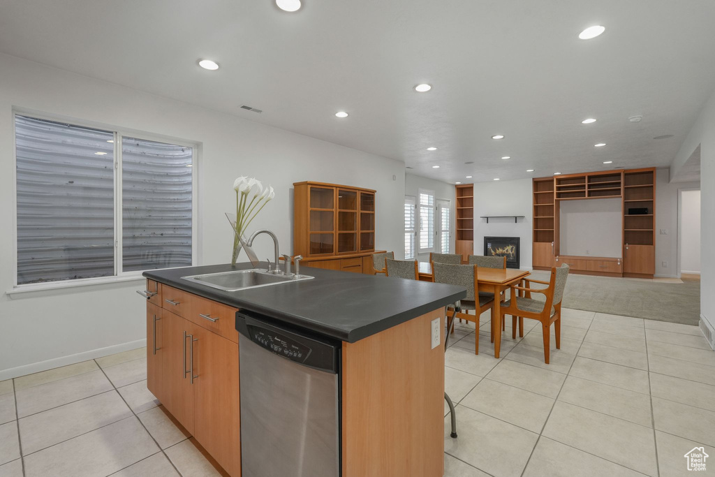 Kitchen featuring stainless steel dishwasher, a sink, dark countertops, light tile patterned flooring, and recessed lighting