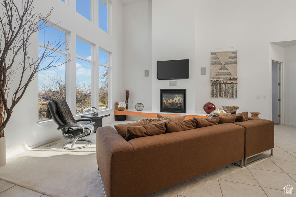 Living room with a high ceiling, light tile patterned flooring, a glass covered fireplace, and baseboards